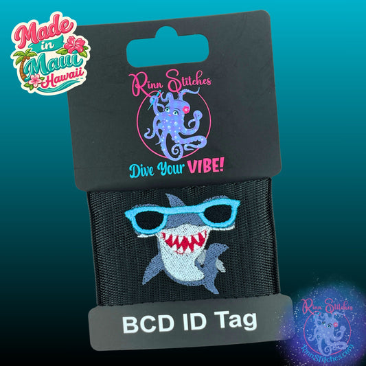 Embroidered BCD Tag with a fun cartoon style Hammerhead shark wearing blue sunglasses on Black Webbing. Made for scuba divers by Rinn Stitches in Maui, Hawaii