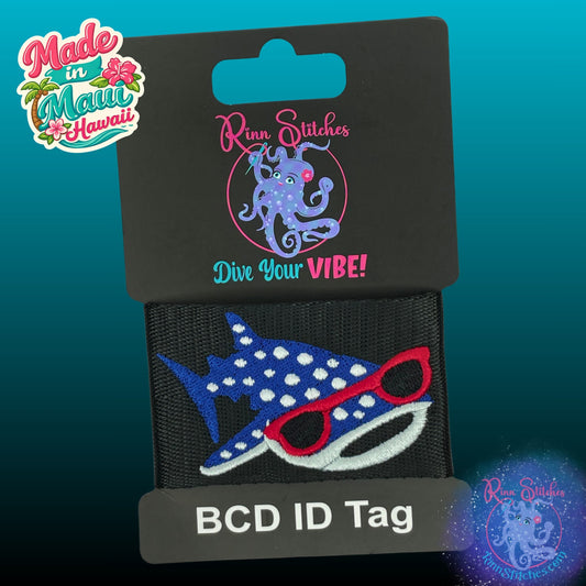 An embroidered BCD ID tag featuring a blue and white spotted whale shark wearing red sunglasses, attached to a black card labeled 'BCD ID Tag' by Rinn Stitches. The image includes a 'Made in Maui Hawaii' logo in the top-left corner.