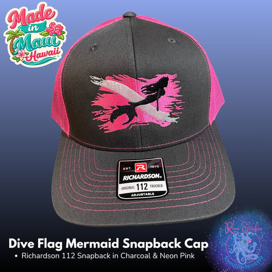A charcoal gray and neon pink snapback cap with a mermaid graphic over a dive flag on the front panel. The cap features a Richardson 112 adjustable snapback sticker on the brim. Made by Rinn Stitches in Maui, Hawaii