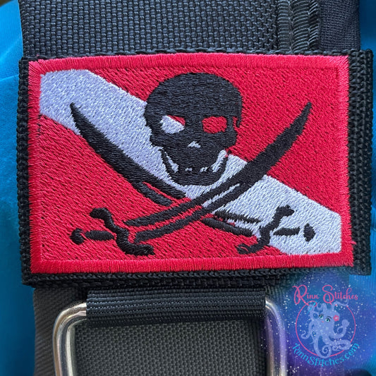 Embroidered BCD Tag with a black skull and crossed swords centered on a red and white dive flag Design on Black Webbing. Made for scuba divers by Rinn Stitches in Maui, Hawaii