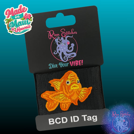 An embroidered orange and yellow Garibaldi  fish BCD ID tag on a black fabric band, attached to a black retail display card. Made by Rinn Stitches on Maui, Hawaii