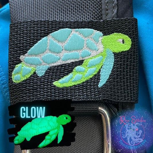 Embroidered BCD Tag Featuring a fully glow-in-the-dark sea turtle design that lights up your gear in low light on Black Webbing. Made for scuba divers by Rinn Stitches in Maui, Hawaii