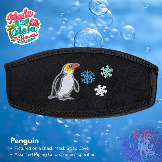 Black mask strap cover featuring an embroidered penguin and three snowflakes in ocean, seafoam, and white, shown against a blue bubbly background with 'Made in Maui Hawaii' by Rinn Stitches