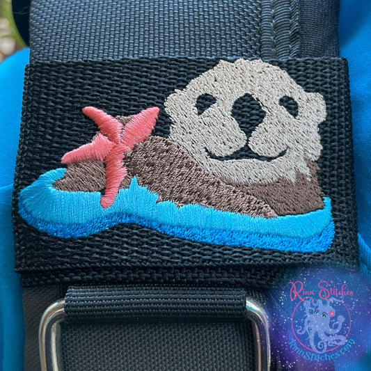 Embroidered BCD Tag with Featuring an adorable sea otter holding a sea star, with a coral colored sea star on Black Webbing. Made for scuba divers by Rinn Stitches in Maui, Hawaii